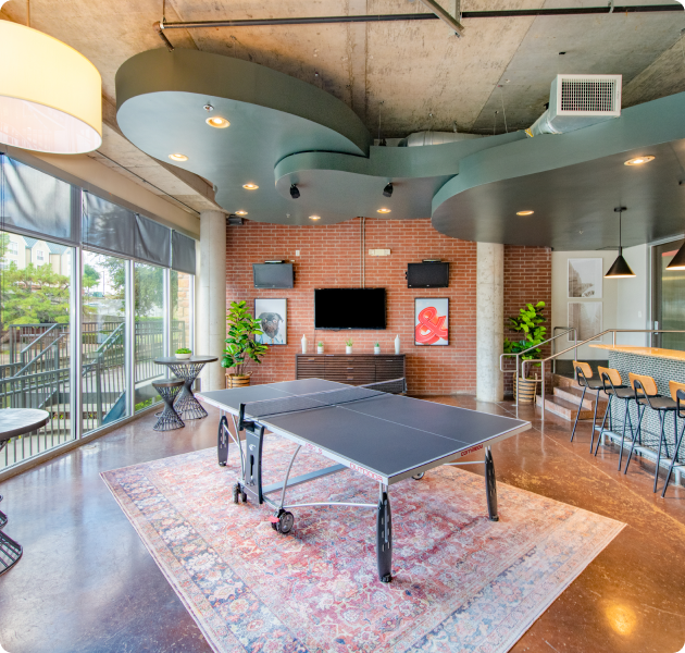 Modern-style community clubhouse with breakfast bar, wall-mounted TV and ping pong game table at MAA Las Colinas luxury apartments in Irving, TX