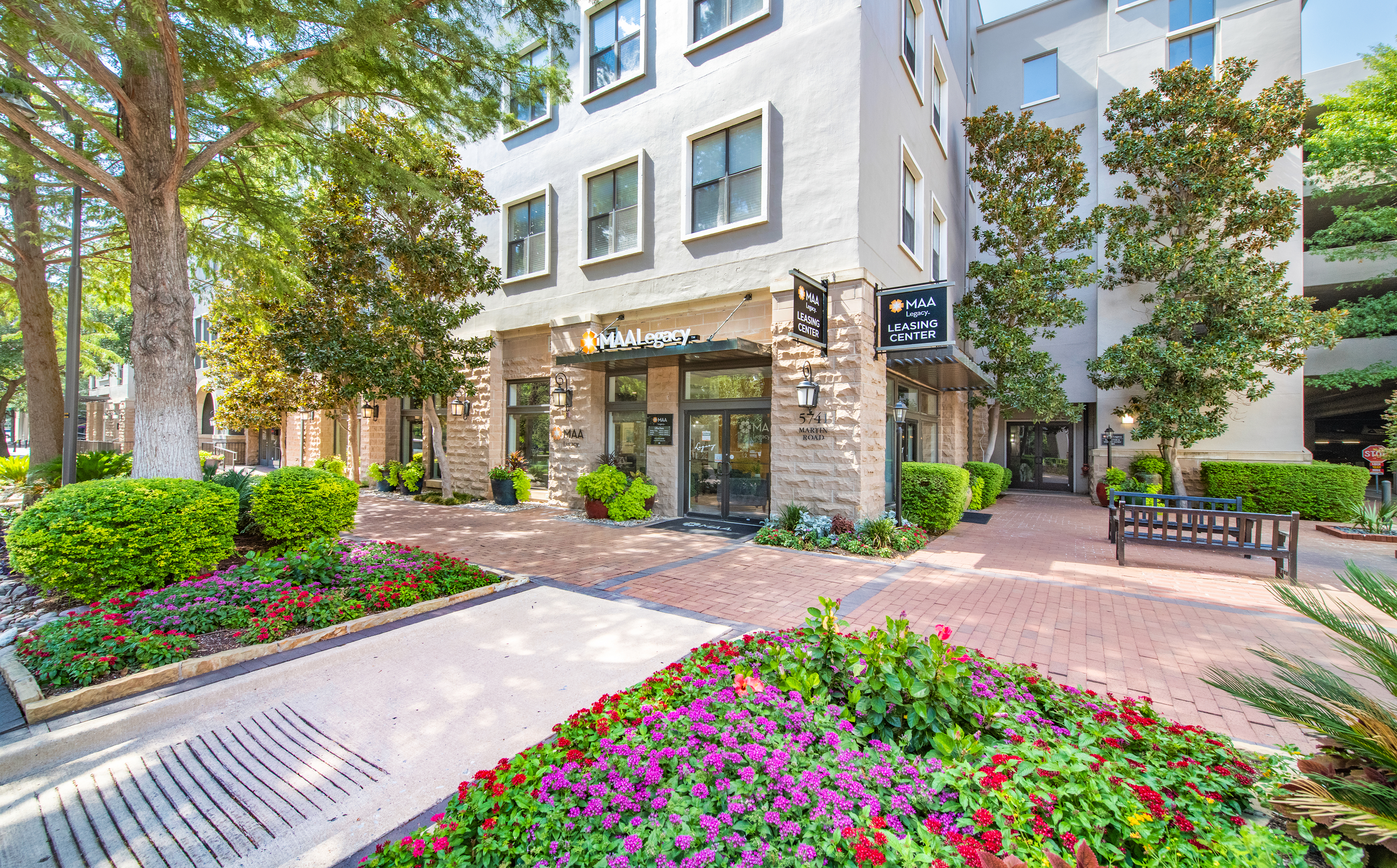 Front signage area walkway with lush bushes and trees next to apartment complex at MAA Legacy luxury apartments in Plano, TX