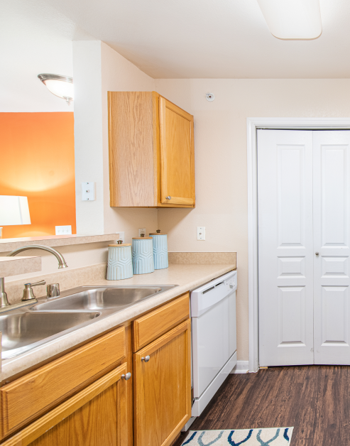 A light-colored kitchen with tan wood cabinets and stainless steel sink and dark hardwood floors at MAA Los Rios luxury apartments in Plano, TX