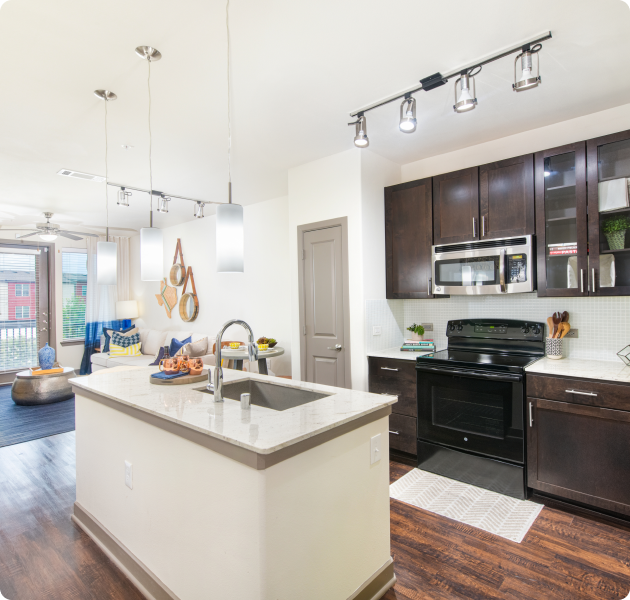Apartment kitchen with granite countertop island and upgraded appliances with faux wood flooring at MAA Market Center luxury apartments in Plano, TX