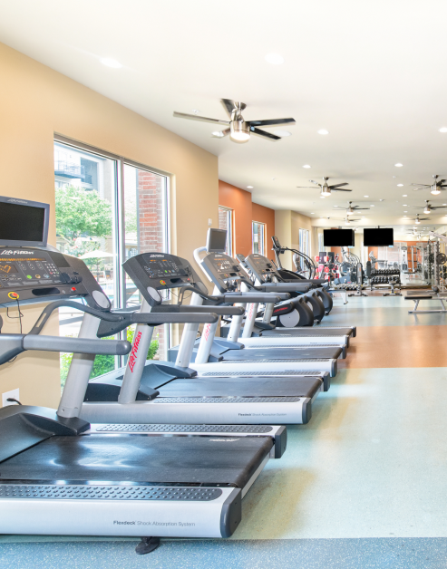 Fitness center with treadmills in natural light next to large windows with workout machines at MAA Market Center luxury apartments in Plano, TX