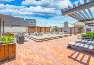 A spacious rooftop patio includes seating areas and planters with brick flooring, plus a wooden deck with string lights under a pergola at MAA McKinney Ave luxury apartments in Dallas, TX