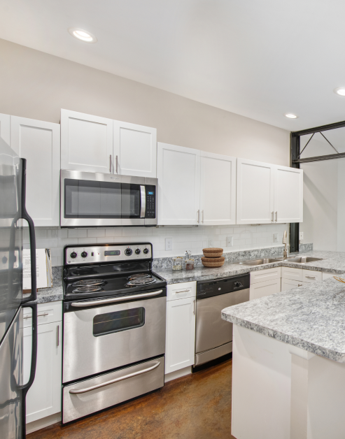 An upscale kitchen equipped with stainless steel appliances complemented by white cabinets and granite countertops at MAA McKinney Ave luxury apartments in Dallas, TX