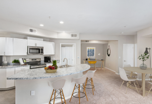 A luxurious light colored kitchen featuring a center island with granite countertops and bar chairs next to open living room area at MAA McKinney Ave luxury apartments in Dallas, TX