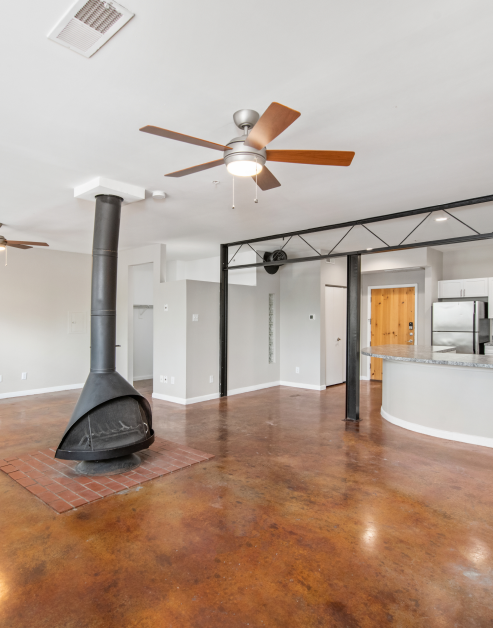 An open-space living room featuring a wood-burning furnace with smoke stack extending to the ceiling, a ceiling fan and cement flooring at MAA McKinney Ave luxury apartments in Dallas, TX