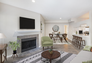 A stylish model living room featuring a small round coffee table with seating area, recessed lighting and wood flooring, next to kitchen bar top counter at MAA McKinney Ave luxury apartments in Dallas, TX