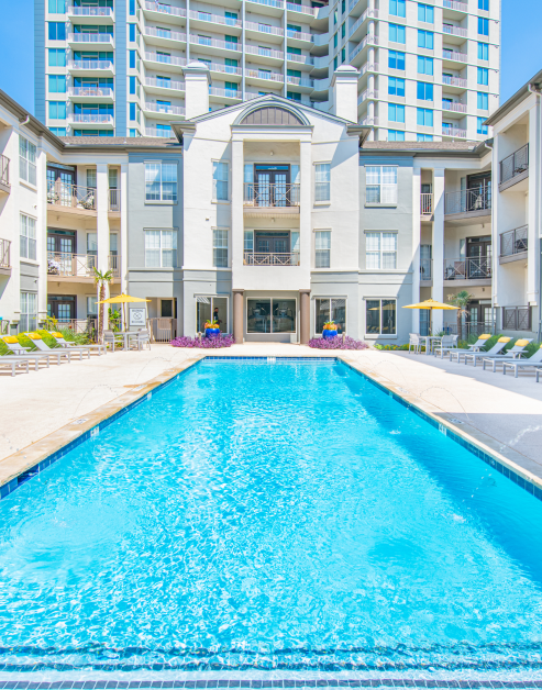 Upscale swimming pool with lounge chairs and patio tables surrounded by the apartment complex at MAA McKinney Ave luxury apartments in Dallas, TX