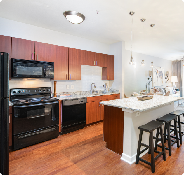 A modern apartment rustic style kitchen featuring black modern appliances, granite bartop counter with bar stools and hanging light fixtures with hardwood flooring at MAA Medical District luxury apartments in Dallas, TX