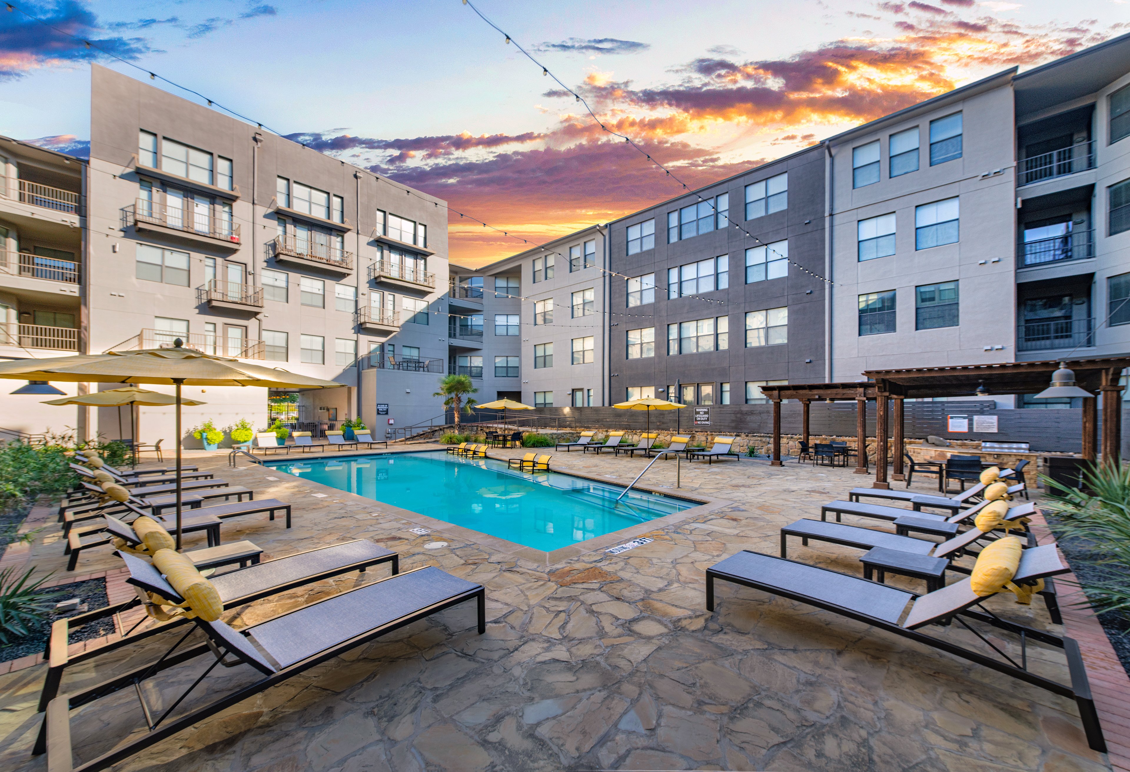 A corner view of a relaxing pool with lounge chairs at sunset at MAA Medical District luxury apartments in Dallas, TX