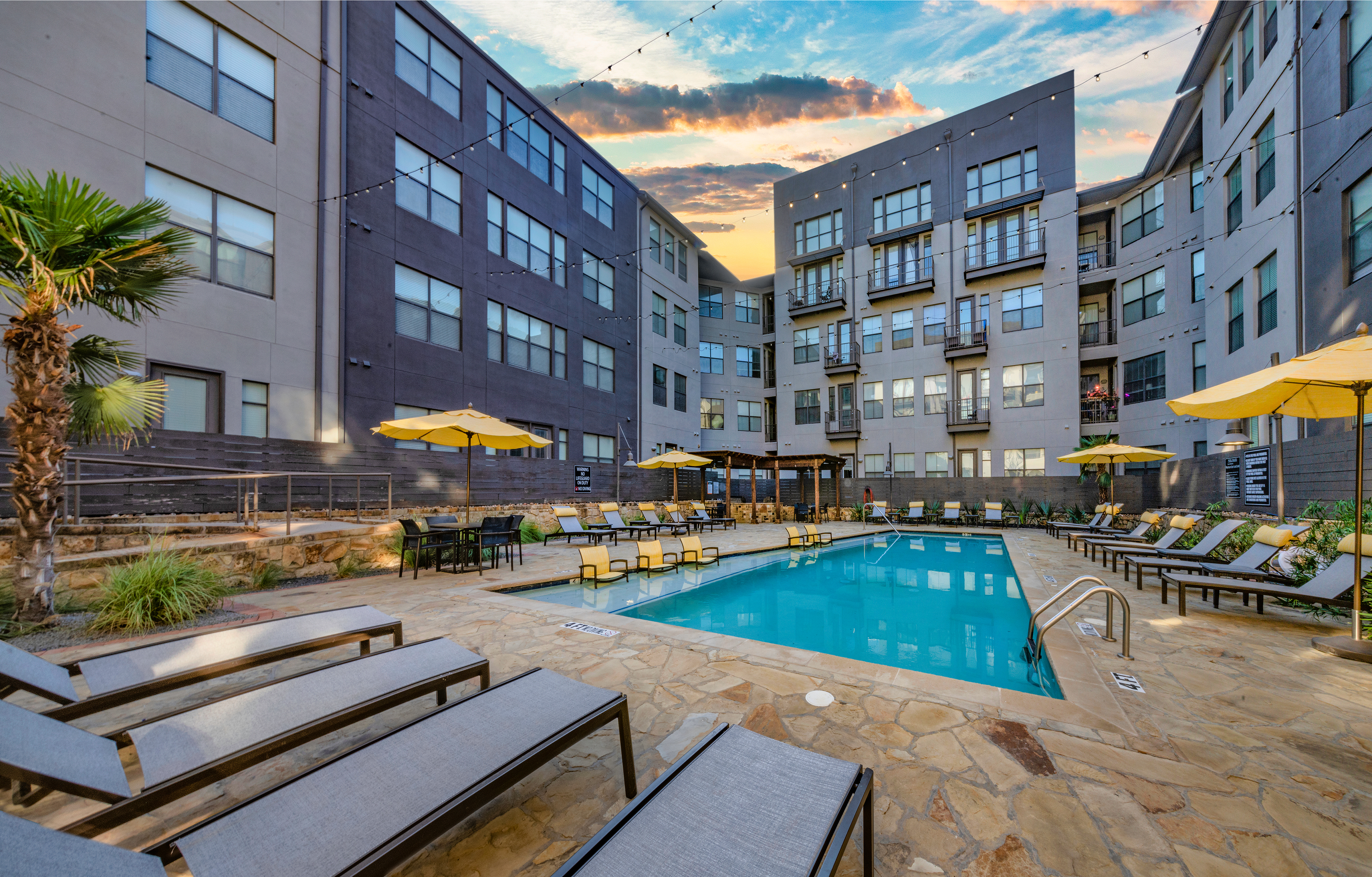 Poolside view of apartment complex with lounge chairs and patio tables at MAA Medical District luxury apartments in Dallas, TX