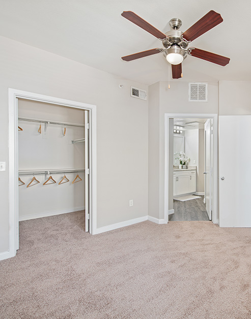 An open-space master bedroom with a ceiling fan, an open view of a large closet and an ensuite bathroom at MAA Medical District luxury apartments in Dallas, TX