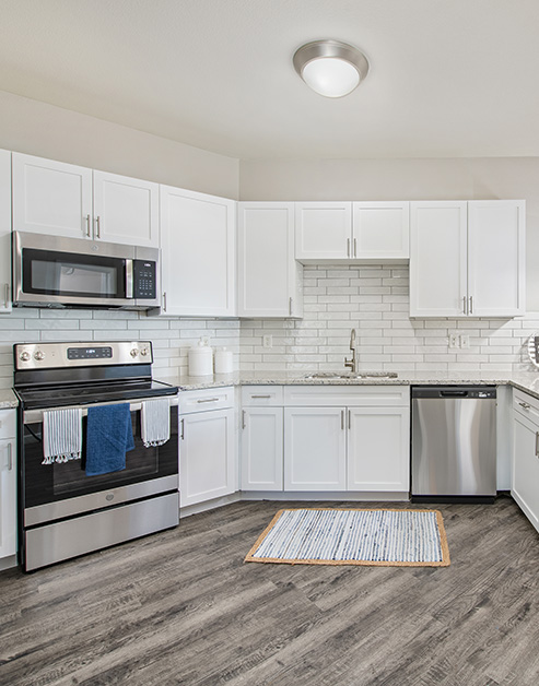 A spacious modern kitchen featuring stainless steel appliances and white cabinets with hard flooring at MAA Medical District luxury apartments in Dallas, TX