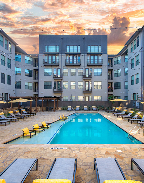 A luxurious pool with a sun deck and poolside lounge chairs with a pergola at MAA Medical District luxury apartments in Dallas, TX