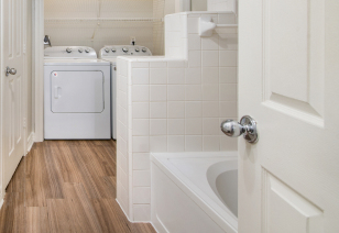 A small bathroom featuring a white washer and dryer, along with a modern white bathtub at MAA Meridian luxury apartments in Dallas, TX