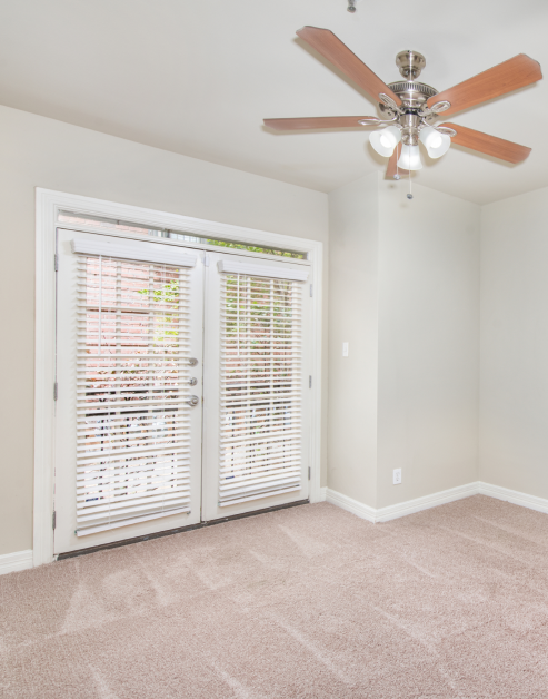 A spacious, unoccupied carpeted bedroom with a ceiling fan and a double French doors at MAA Meridian luxury apartments in Dallas, TX