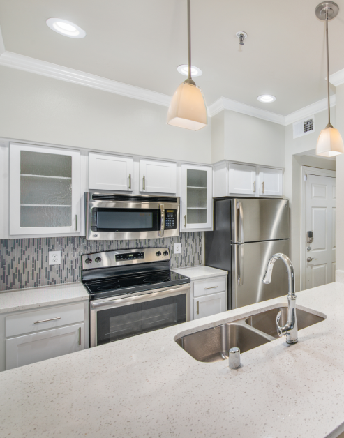 A stylish kitchen featuring stainless steel appliances, granite countertops, white cabinets with glass doors, hanging light fixtures and high ceilings at MAA Meridian luxury apartments in Dallas, TX