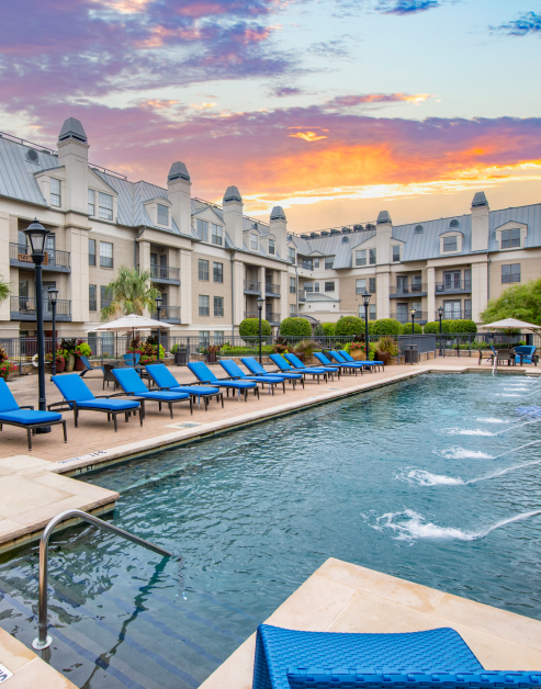 A spacious swimming pool with lounge chairs featuring blue cushions and beautiful sunset views at MAA Meridian luxury apartments in Dallas, TX