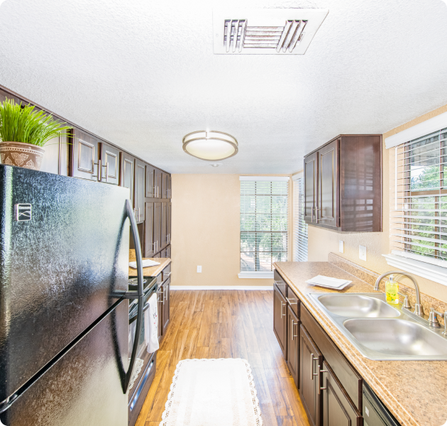An apartment kitchen features dark wood cabinets with granite countertops and modern appliances, a round light fixture and wood flooring at MAA Remington Hills luxury apartments in Irving, TX