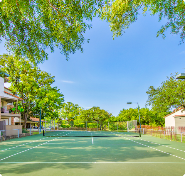 A gated tennis court next to the apartment complex surrounded by trees at MAA Remington Hills luxury apartments in Irving, TX
