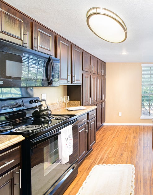 An upscale kitchen features dark wood cabinets with granite countertops and modern appliances, a round light fixture and wood floors at MAA Remington Hills luxury apartments in Irving, TX