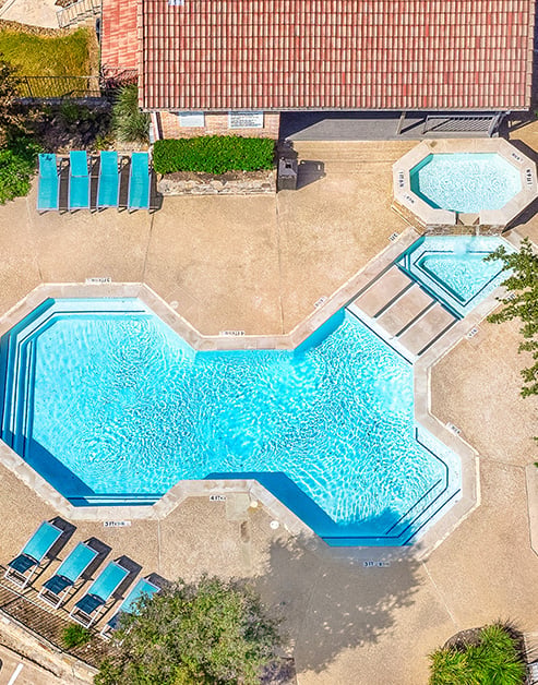 Swimming pool with steps with lounge chairs surrounded by large trees at MAA Remington Hills luxury apartments in Irving, TX