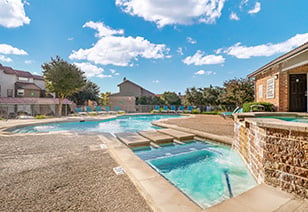A side view of a resort-style swimming pool with lounge chairs and trees at MAA Remington Hills luxury apartments in Irving, TX
