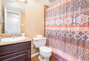 A upscale bathroom with a colorful shower curtain and bathtub next to vanity mirror with granite countertop and dark wood cabinets at MAA Remington Hills luxury apartments in Irving, TX