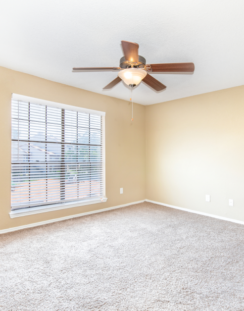 An open space empty bedroom with large window and blinds and carpet floors at MAA Remington Hills luxury apartments in Irving, TX