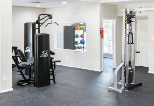 An modern fitness center features weight machine stations next to a studio fitness room with a window at MAA Remington Hills luxury apartments in Irving, TX