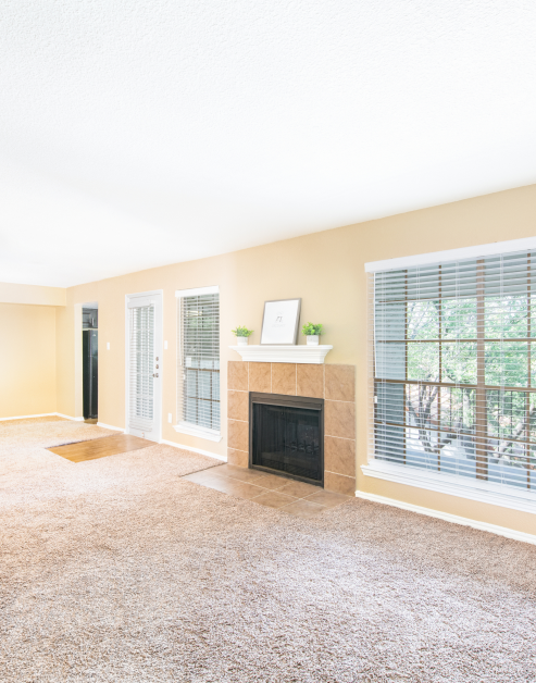 A spacious empty living room with a fireplace and side windows and blinds next to a French door entrance at MAA Remington Hills luxury apartments in Irving, TX