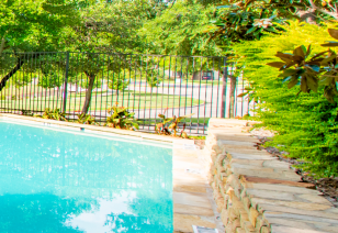 A close-up view of the gated swimming pool edge with a brick wall surrounded by trees and bushes at MAA Remington Hills luxury apartments in Irving, TX