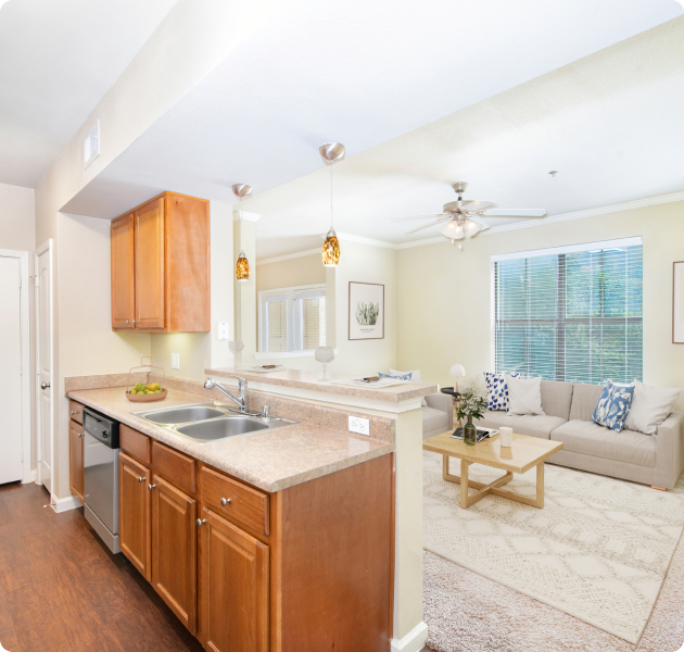 A luxurious apartment kitchen adjacent to the living room featuring wooden cabinets, hanging light fixtures and a ceiling fan, with a couch with a coffee table at MAA Starwood luxury apartments in Frisco, TX