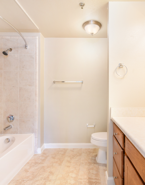 A luxurious bathroom with wooden cabinets, a bathtub with tile flooring and bright lighting at MAA Starwood luxury apartments in Frisco, TX