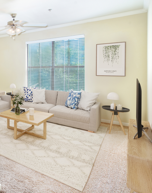 A model living room featuring a couch, a coffee table and ceiling fan with a large picture window at MAA Starwood luxury apartments in Frisco, TX