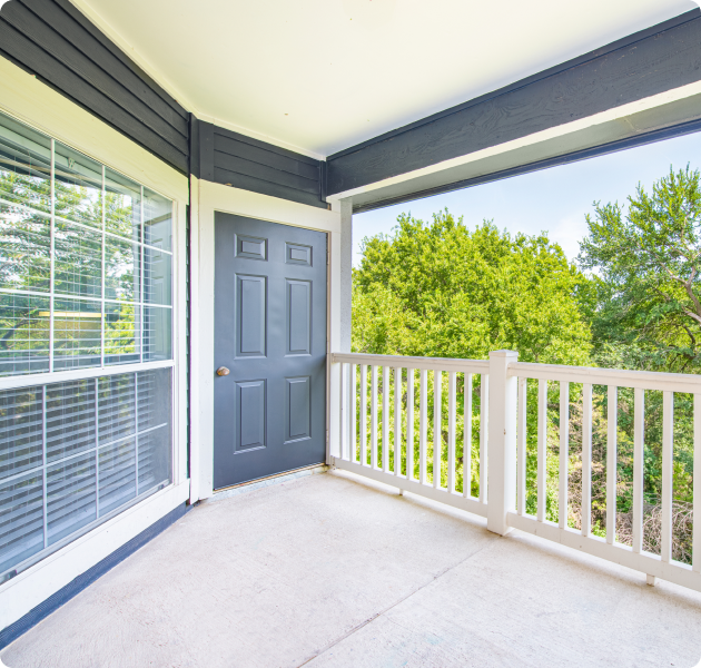 An apartment front porch with white fencing, blue entrance door with large windows overlooking lush trees at MAA Stonebridge Ranch luxury apartments in McKinney, TX