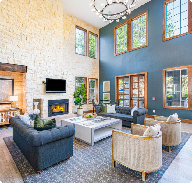 Spacious community lounge area with high ceilings and large windows, light stone fireplace wall, blue sofas and armchairs with a coffee table at MAA Stonebridge Ranch luxury apartments in McKinney, TX