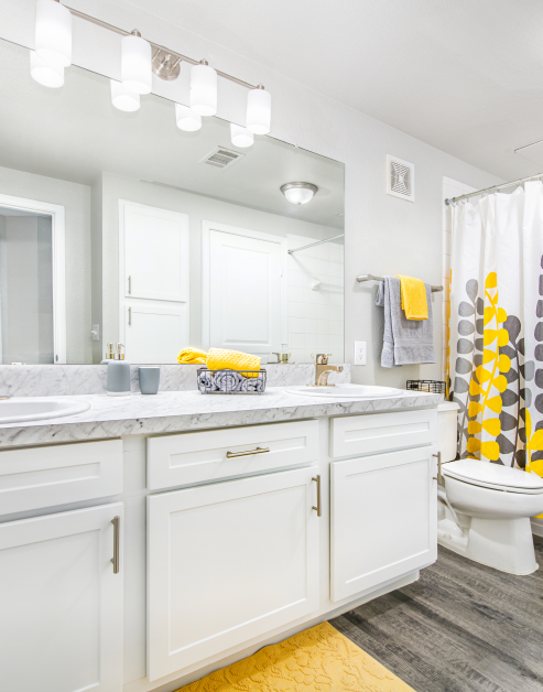 A modern bathroom features white cabinets, large vanity mirror with double sinks and elegant lighting fixtures at MAA Stonebridge Ranch luxury apartments in McKinney, TX