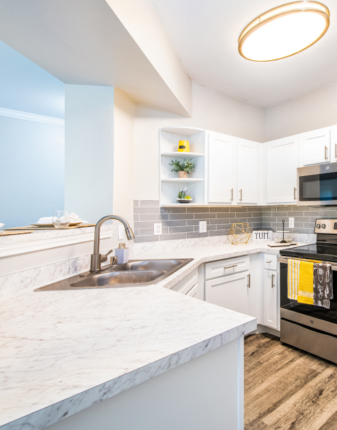 An upscale kitchen with white cabinets and countertops, stainless steel appliances with a bar top counter at MAA Stonebridge Ranch luxury apartments in McKinney, TX
