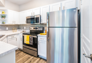 Modern kitchen with white cabinets, wood flooring and a stainless steel refrigerator at MAA Stonebridge Ranch luxury apartments in McKinney, TX