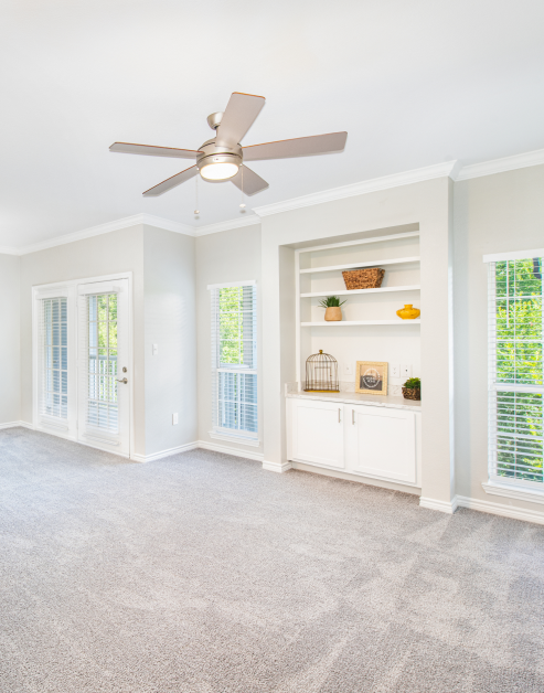 Spacious open-layout carpeted living room, featuring a stylish ceiling fan, French doors and built-in shelving at MAA Stonebridge Ranch luxury apartments in McKinney, TX