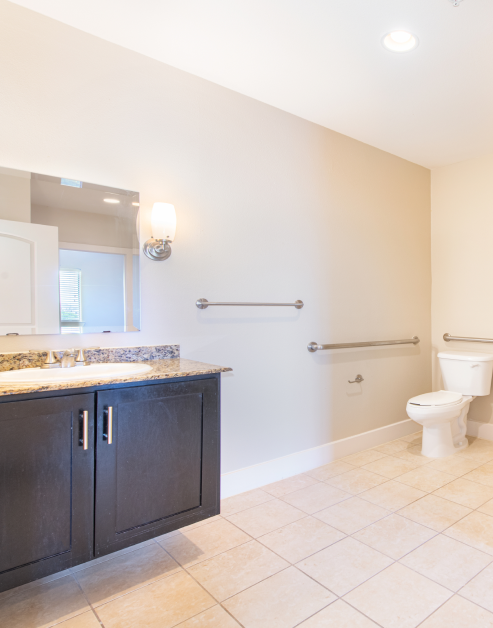 An upscale bathroom featuring a vanity mirror and granite countertops with dark wooden cabinets at MAA Times Square luxury apartments in McKinney, TX