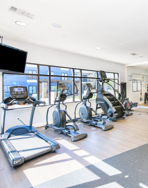 The fitness center equipped with treadmills, ellipticals machine and a wall mounted TV at MAA Times Square luxury apartments in McKinney, TX