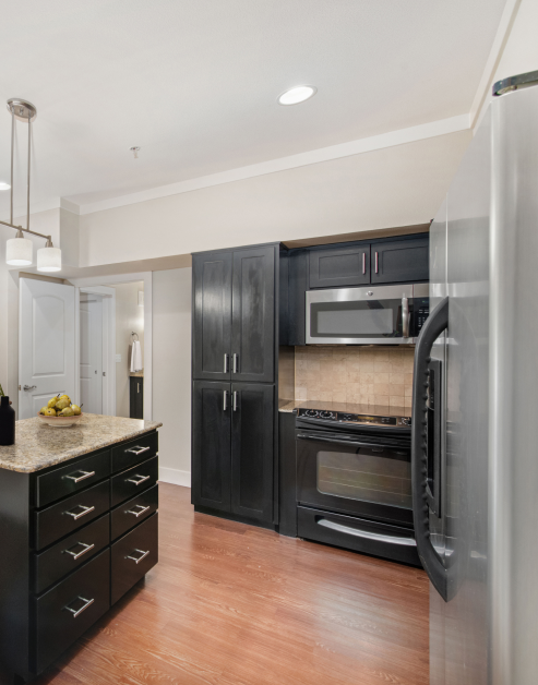 A modern kitchen with a granite countertop, dark wood cabinets and light wood flooring at MAA Times Square luxury apartments in McKinney, TX
