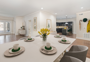 A modern kitchen with wood flooring, next to a dining area featuring a table and chairs illuminated by recessed ceiling lights at MAA Times Square luxury apartments in McKinney, TX
