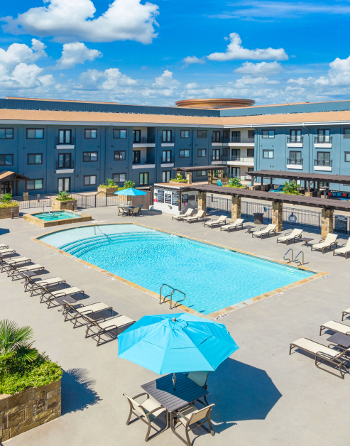 Gated resort-style pool with lounge chairs and patio tables at MAA Times Square luxury apartments in McKinney, TX