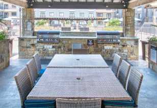An outdoor grill station under a pergola with large tables with two stainless steel grills at MAA Times Square luxury apartments in McKinney, TX
