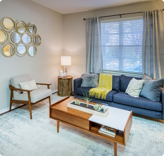 An apartment model living room with stylish blue couch, coffee table with natural lighting at MAA Uptown Village luxury apartments in Dallas, TX