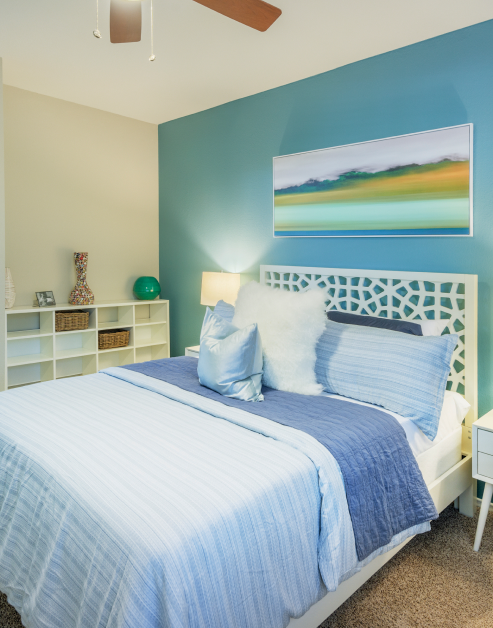 Model blue-toned bedroom with landscape wall painting and ceiling fan at MAA Uptown Village luxury apartments in Dallas, TX