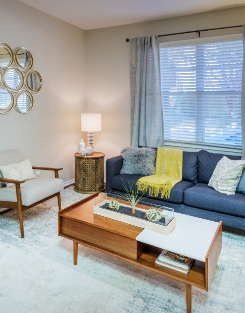 Carpeted model living room with a modern-style couch and wooden coffee table with armchair at MAA Uptown Village luxury apartments in Dallas, TX