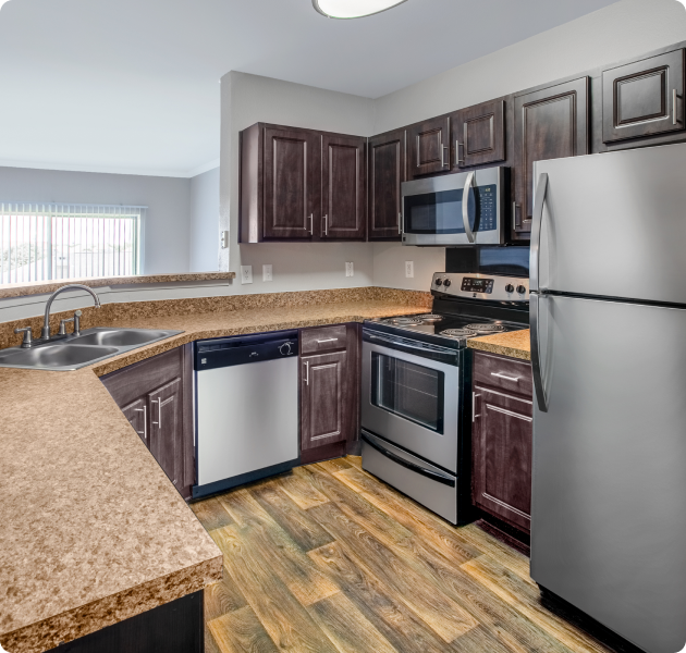 An apartment kitchen with dark brown cabinets, stainless steel appliances and wood flooring at MAA Valley Ranch luxury apartments in Irving, TX
